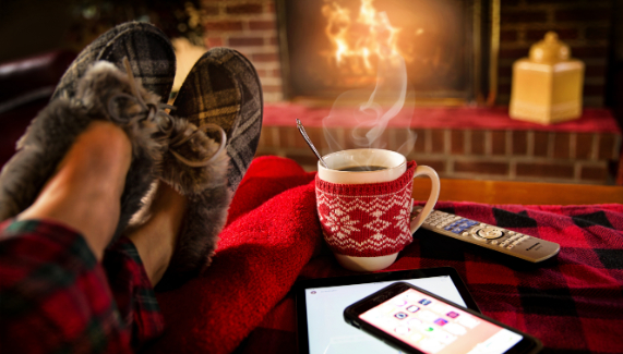 Someone with a steaming cup of hot chocolate getting warm by the fireplace