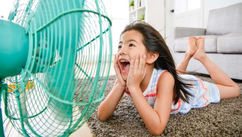 A girl sits in front of a fan to cool down