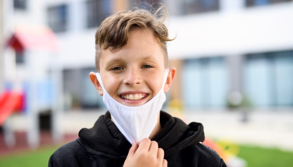A young student wears a mask at school