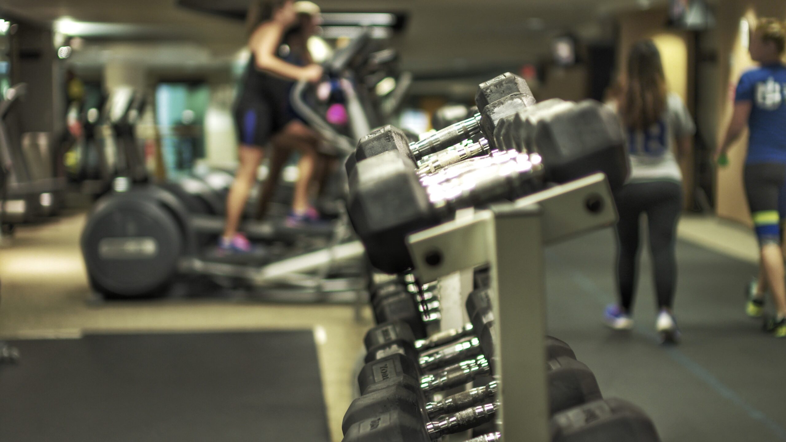 Dumbbells rack with people background gym scaled