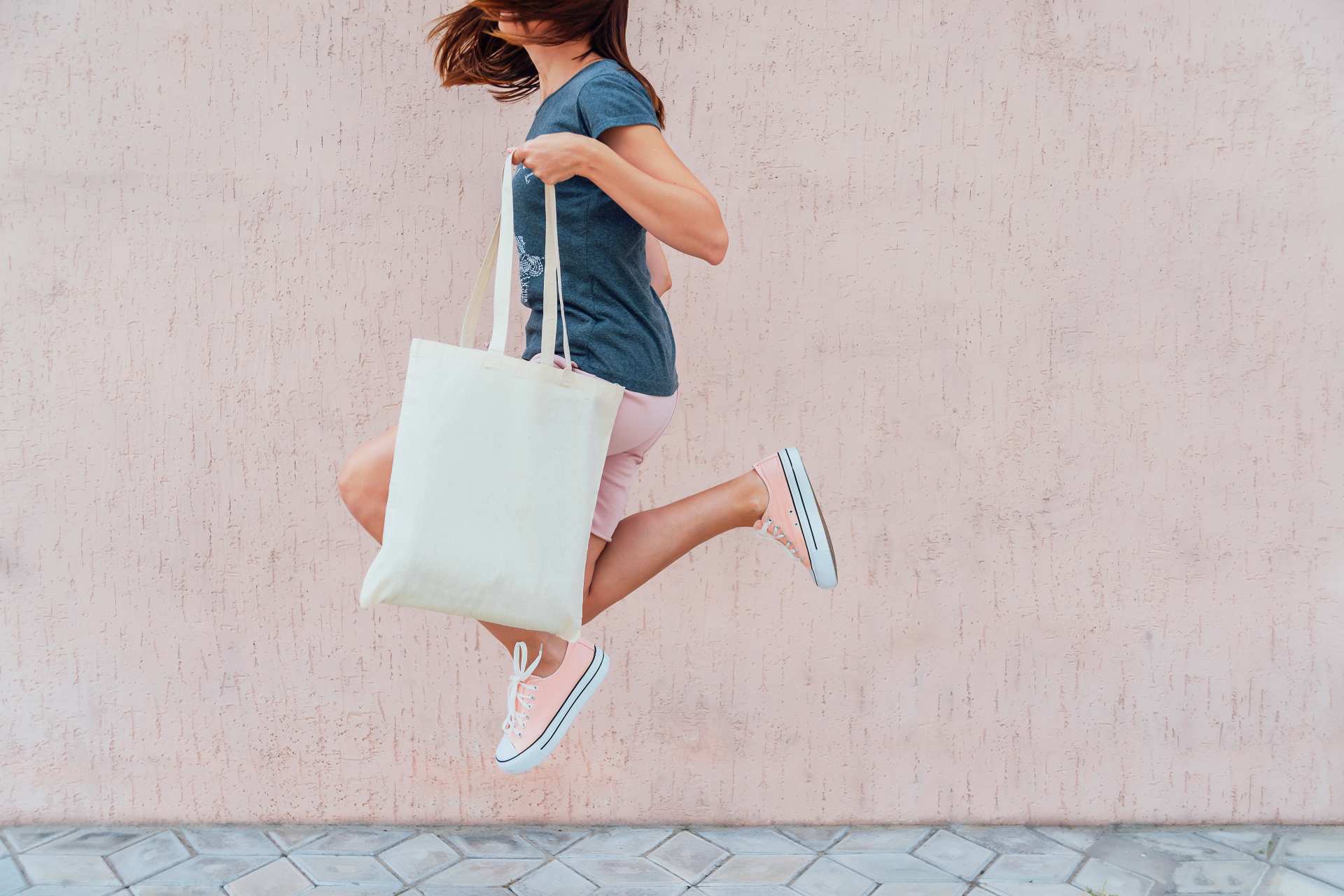 9 Nifty Tips To Reduce Your Plastic Pollution 1 A woman jumping while holding a reusable canvas tote