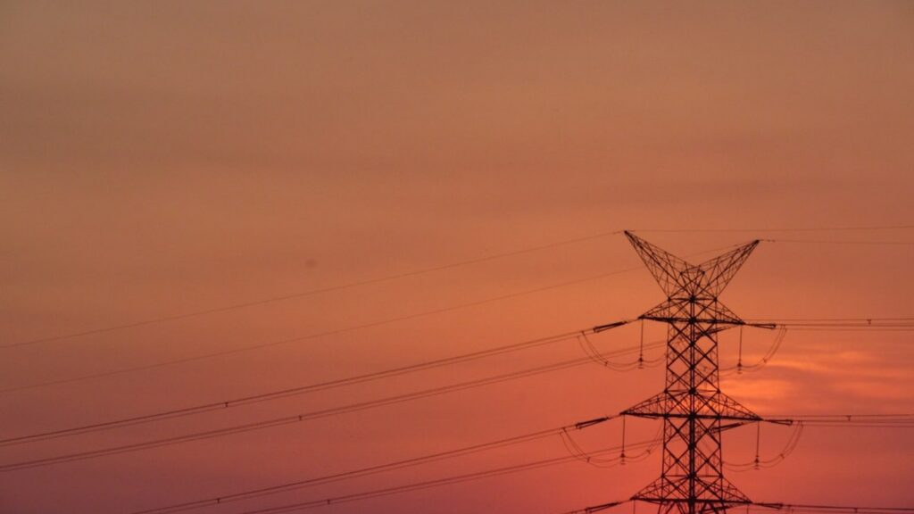 Electricity transmission pylon silhouetted against a Texas sunset representing rising grid demand