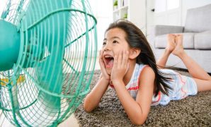 A girl sits in front of a fan to cool down