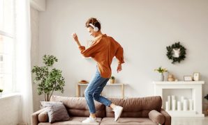 Cheerful woman listening to music and dancing on soft couch at home in day off
